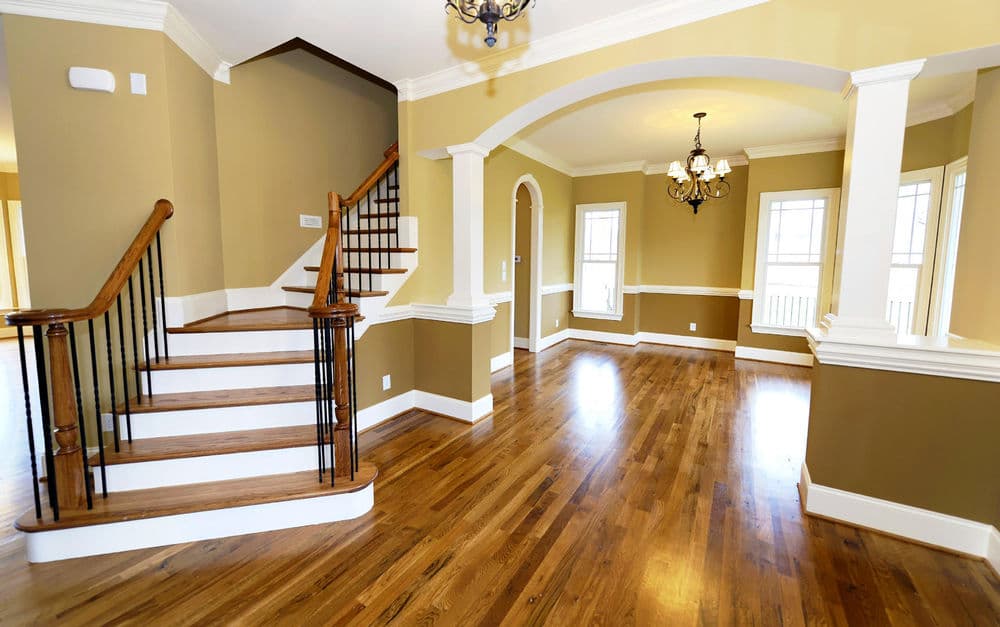 White staircase post with decorative trim, surrounded by construction materials and plastic sheeting.